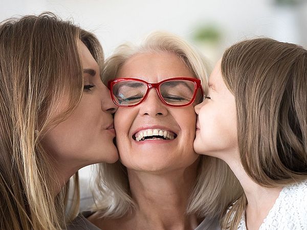 Eine glückliche ältere Frau wird von ihrer Tochter und ihrer Enkeltochter auf die Wange geküsst.