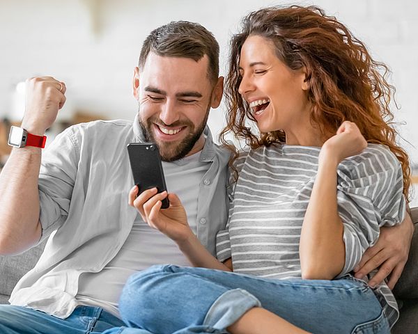 Mann und Frau schauen auf Smartphne und lachen und freuen sich.