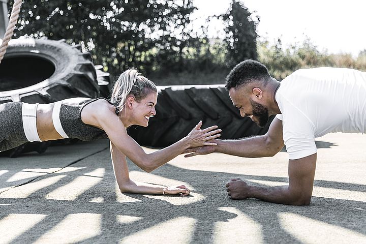 Eine junge blonde Frau und ein junger Mann planken auf Asphalt und klatschen dabei ab. 