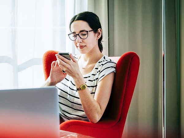 Eine junge Frau sitzt auf einem Stuhl und tippt auf ihr Smartphone.