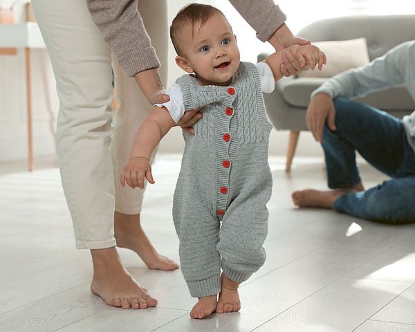 Baby macht erste Schritte an den Händen seiner Mama.