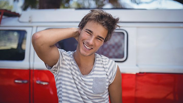 Ein junger Mann lächelt in die Kamera und steht dabei vor einem Kleinbus 
