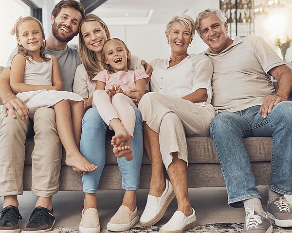 Drei Generationen Familie sitzen zusammen auf einem Sofa und sehen glücklich aus.